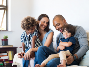 family sponsored immigration - image of multicultural family, mum, dad and two kids smiling on the couch - call HCM Legal today